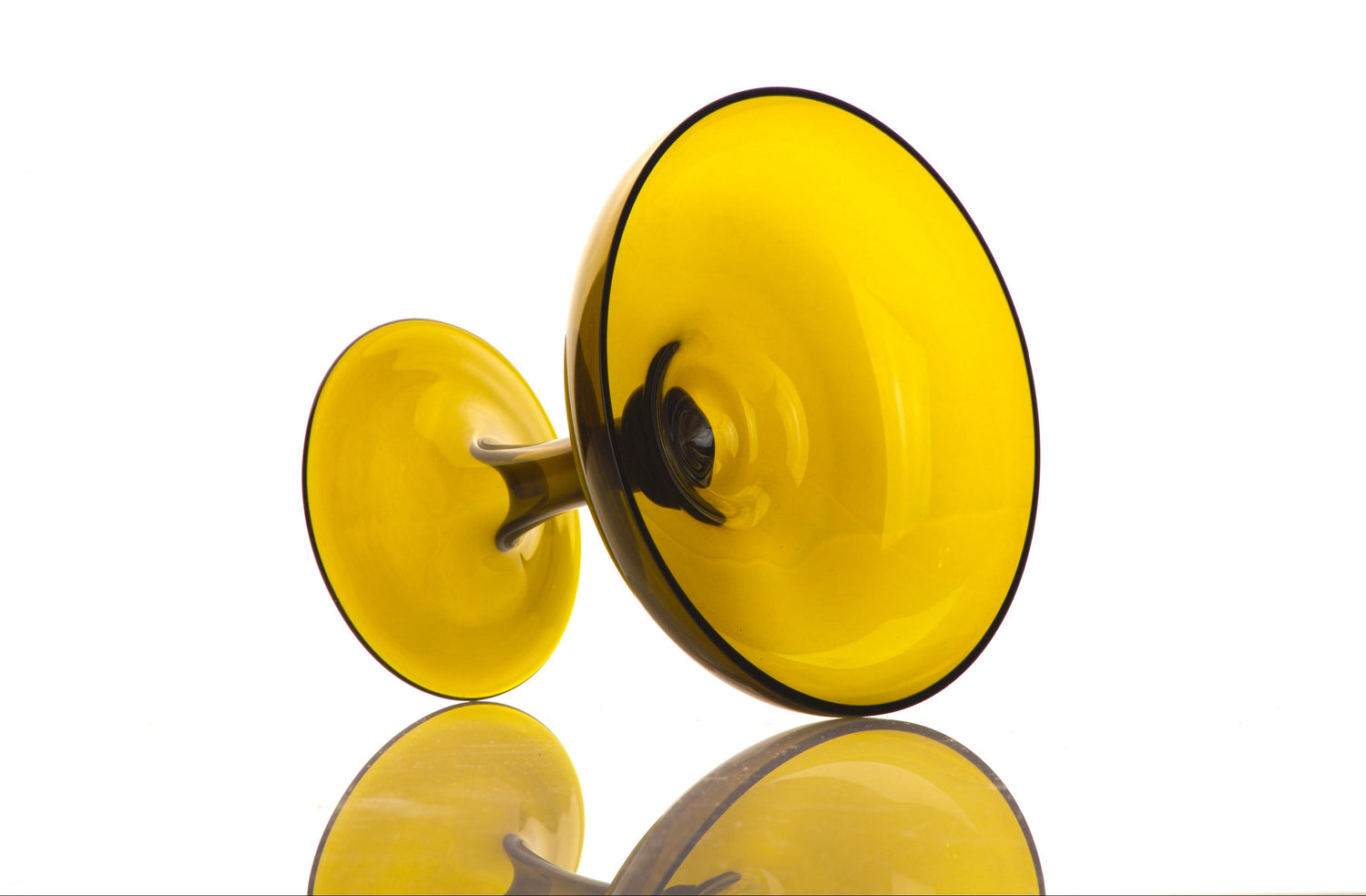 A translucent yellow glass goblets with dark rims, shown from a side angle on a reflective white surface against a white background. Made from recycled glass 